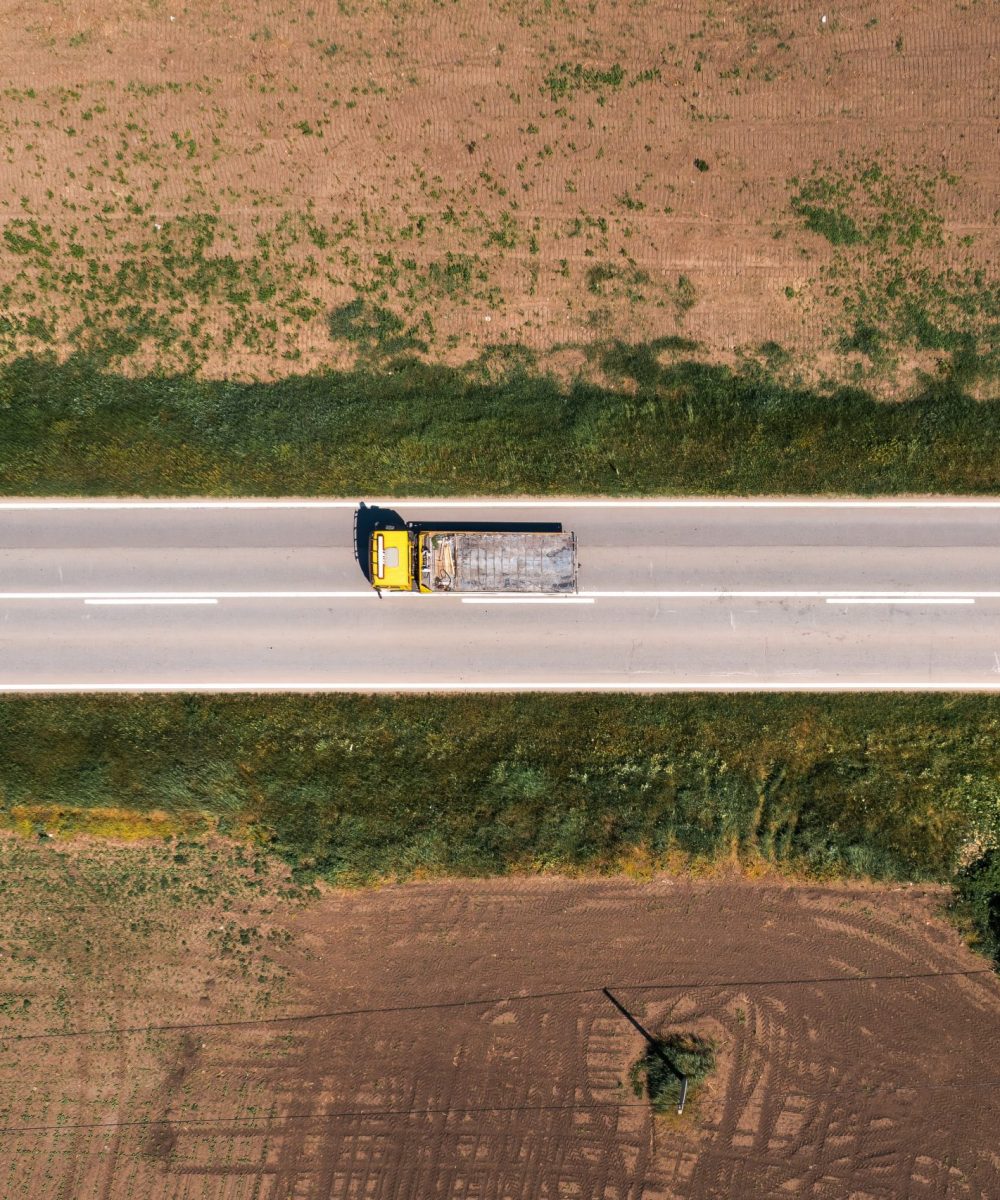 Industrial dump truck with empty trailer on highway through countryside landscape, drone pov aerial shot directly above on sunny springtime day. Industry and transport concept.