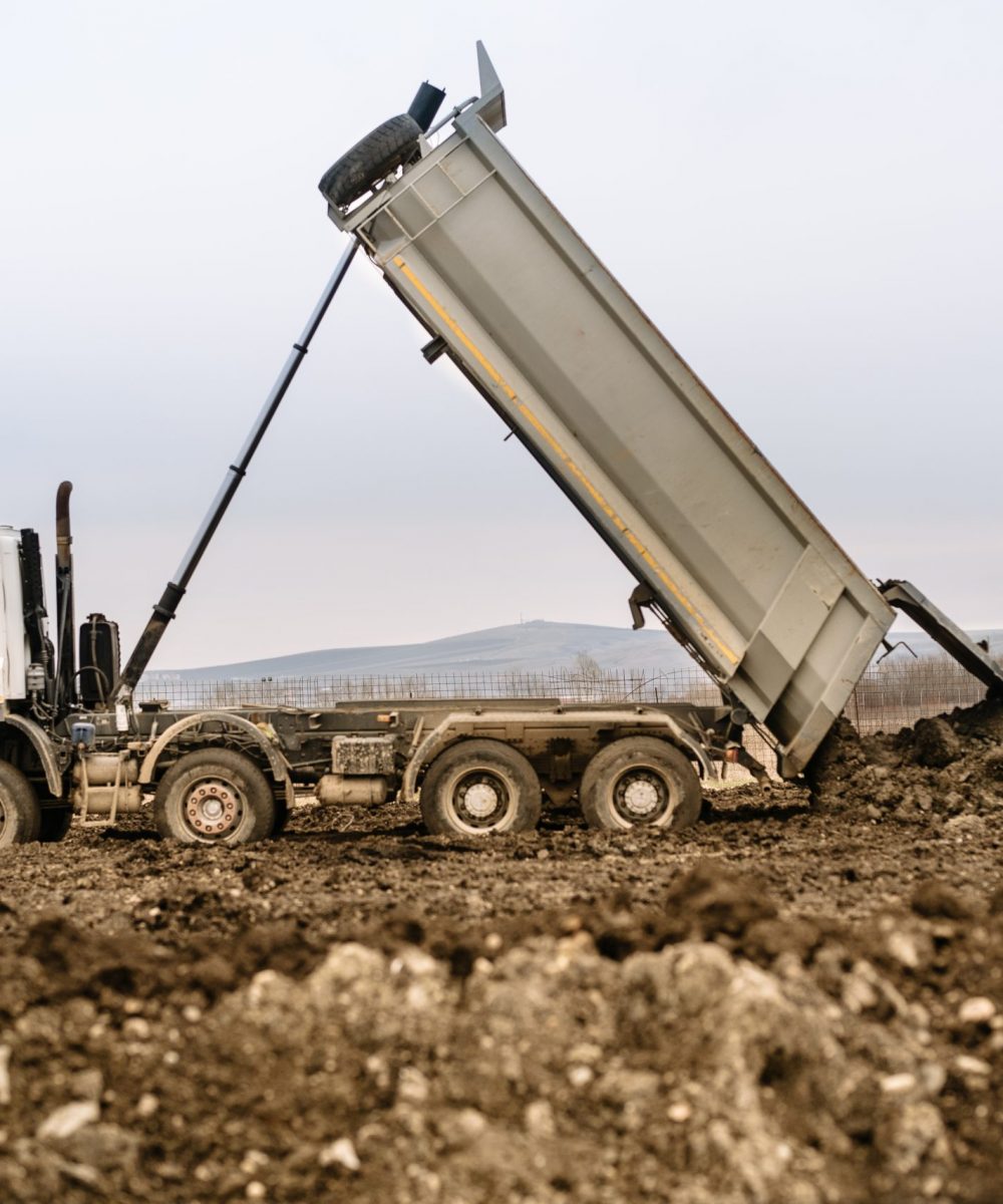 Industrial dumper truck un loading gravel and earth at highway construction site